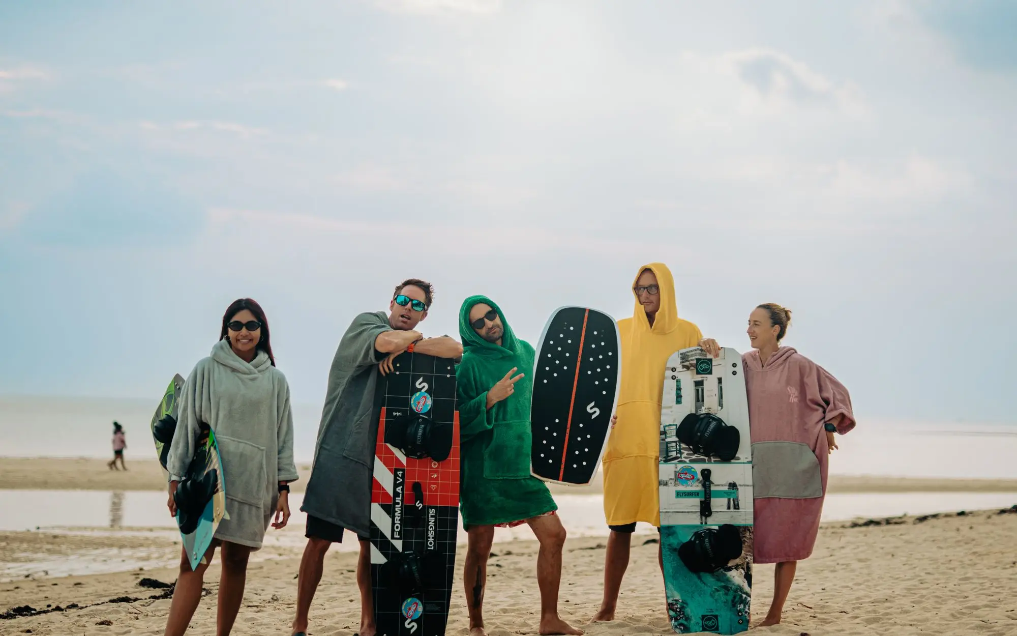 Five friends standing together on the beach with their kiteboards